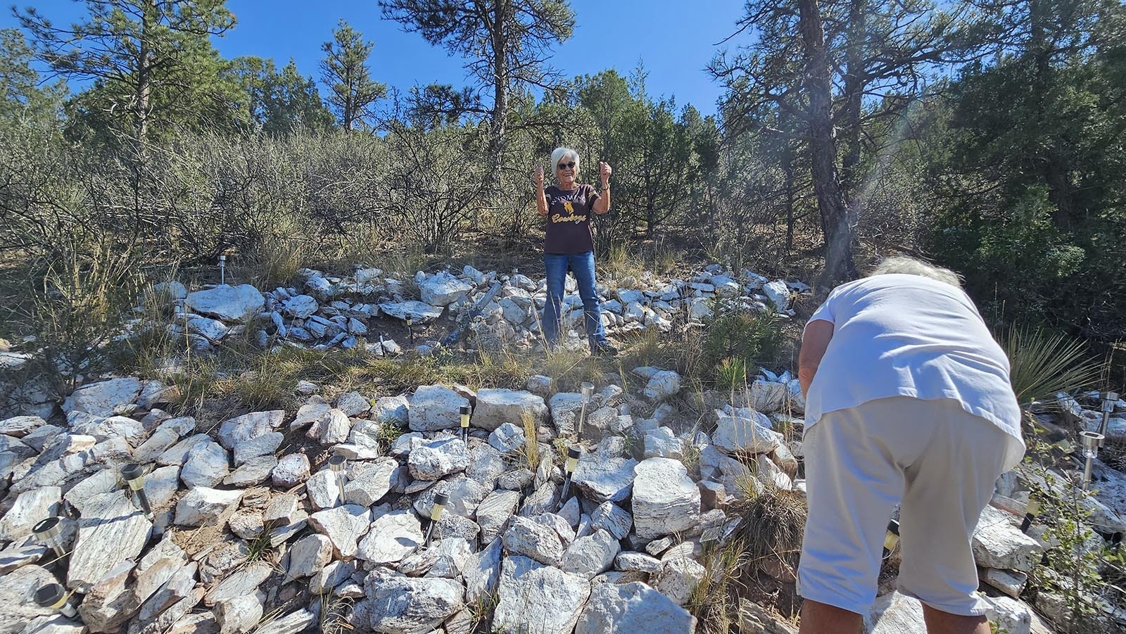 Angelina Neider, Ray Monsold's sister, pumps her fists, excited to show that she made it up the hill to help repaint the white "S" for Sunrise, while Kathy Troupe, in the foreground, continues painting rocks with a white spray can.