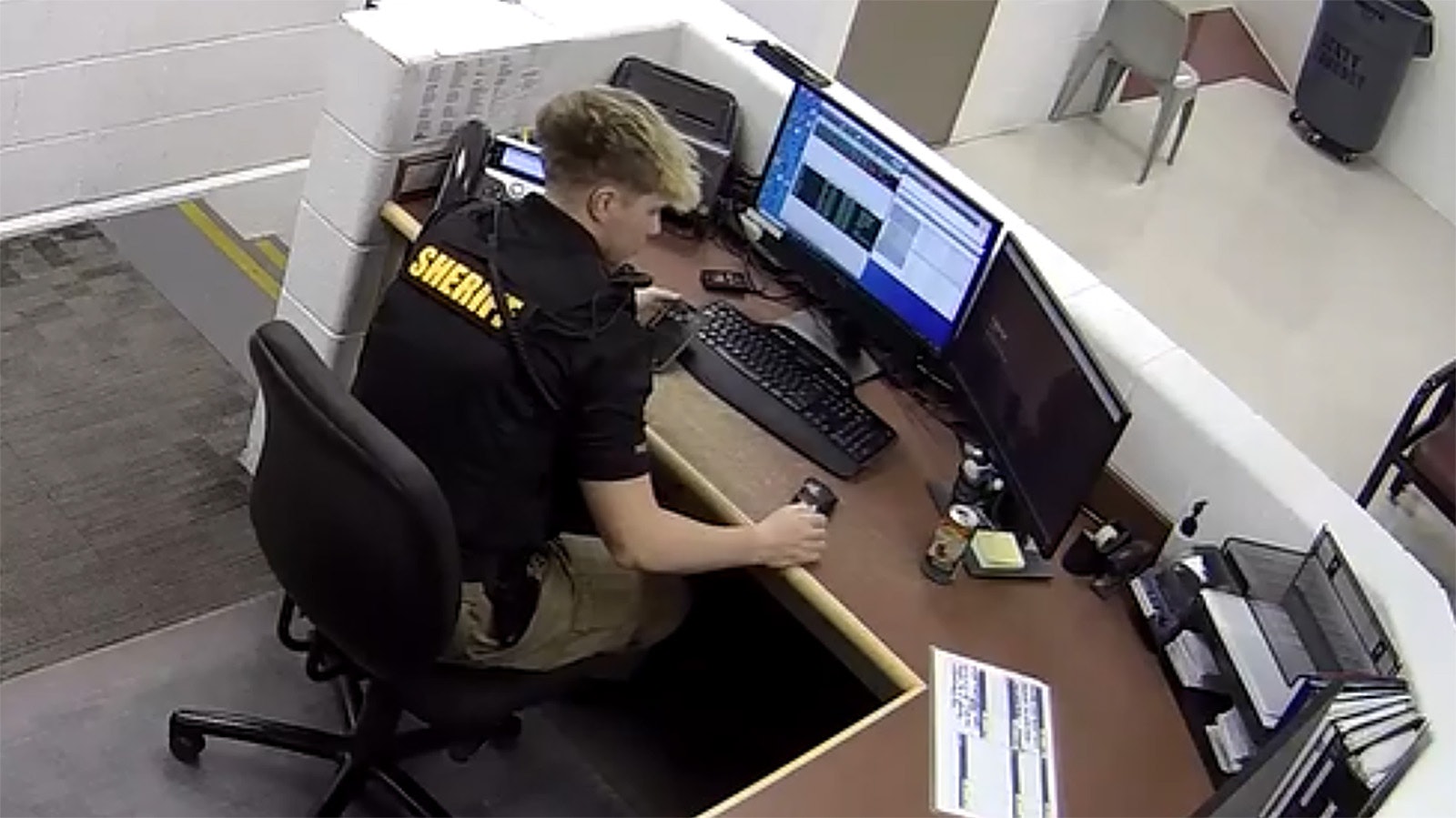 In this screenshot from video, a Sweetwater County Sheriff's Office Detention Center employee reacts after his can of soda slides on the desk without being touched.