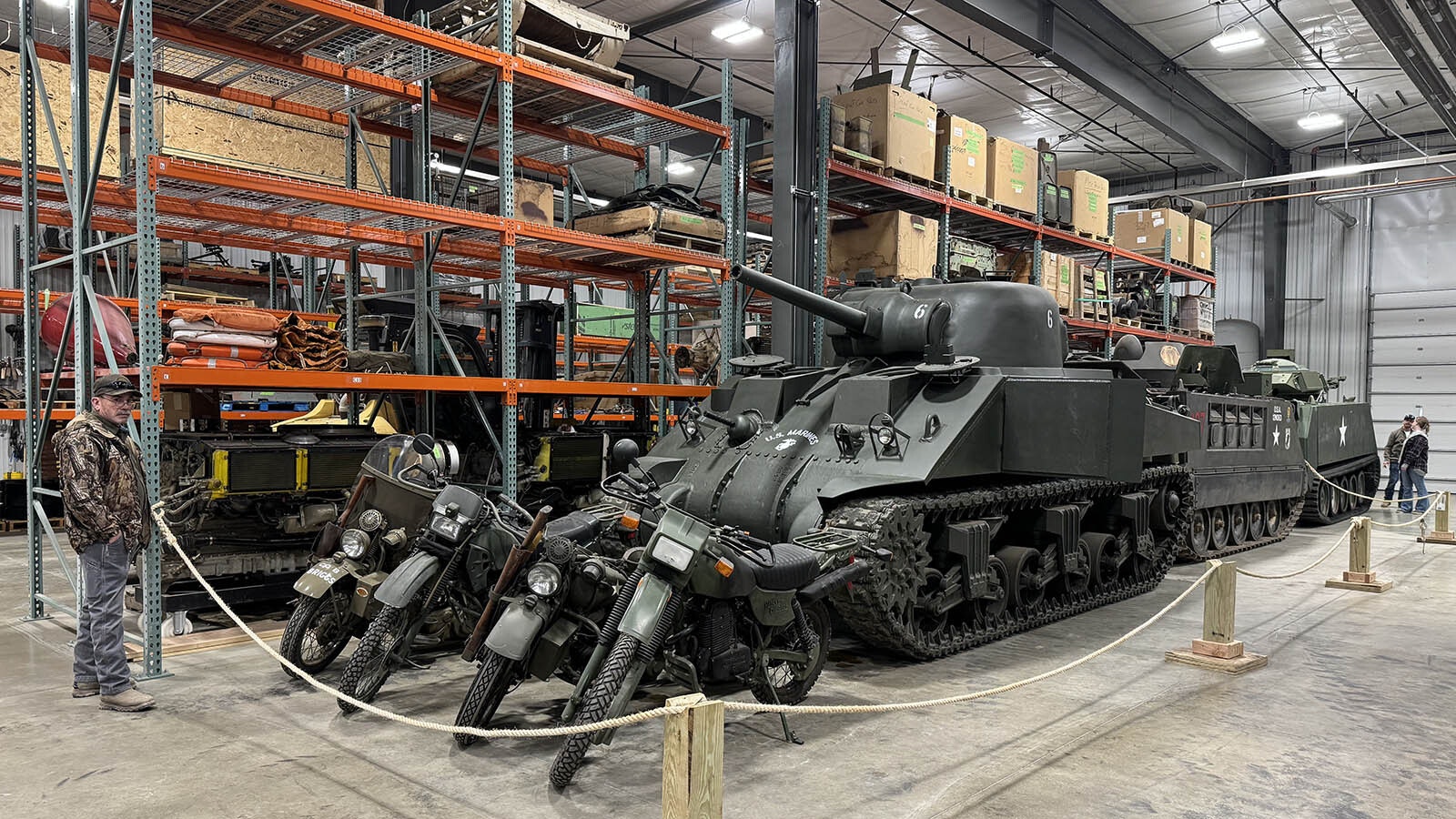 Motorcycles, a Sherman tank and other military vehicles parked along the shelves in the tank restoration shop's storage facility.