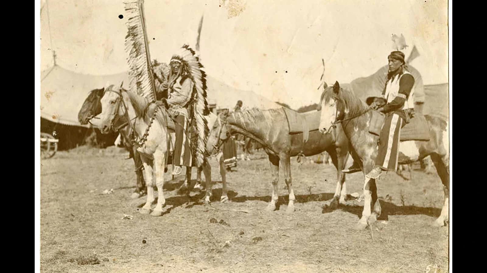 Chief Iron Tail holds a coup stick on horseback in 1912, with Buffalo Bill’s Wild West tents in the background.