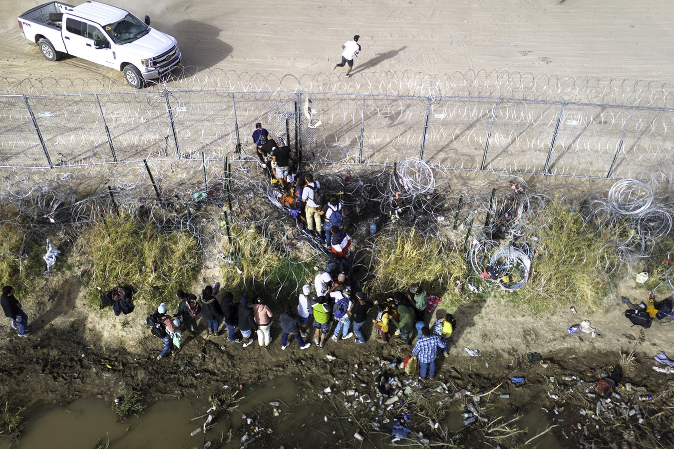 In an aerial view, immigrants pass through coils of razor wire while crossing the U.S.-Mexico border on March 13, 2024, in El Paso, Texas. The wire was placed by the troops as part of Texas Gov. Greg Abbott's "Operation Lone Star" to deter migrants from crossing into Texas.