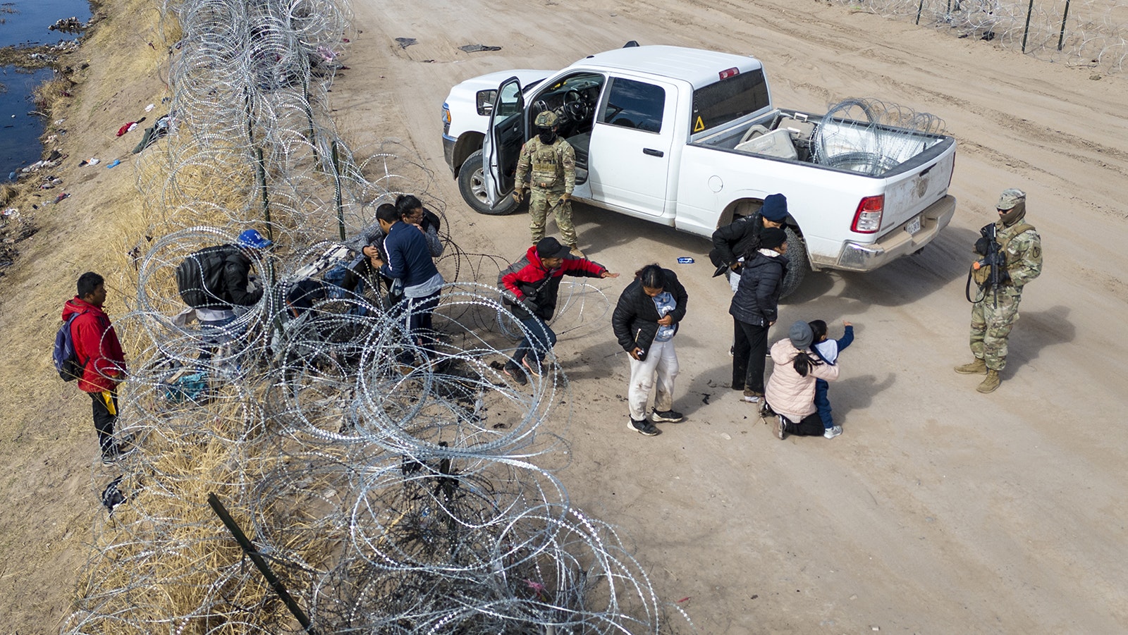 Seen from an aerial view, Texas National Guard troops watch as immigrants pass through razor wire after crossing the U.S.-Mexico border into El Paso, Texas, on Jan. 31, 2024, from Ciudad Juarez, Mexico.