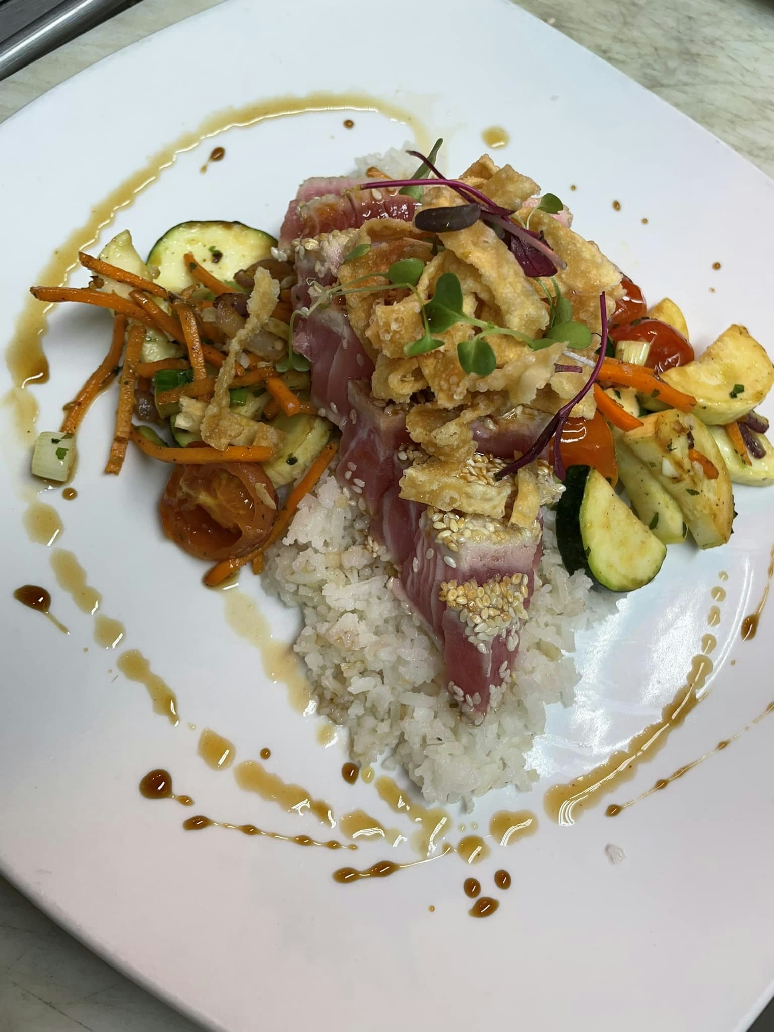 Sesame-crusted ahi with steamed white rice stir-fry veggies citrus polnzu soy reduction and wonton strips.