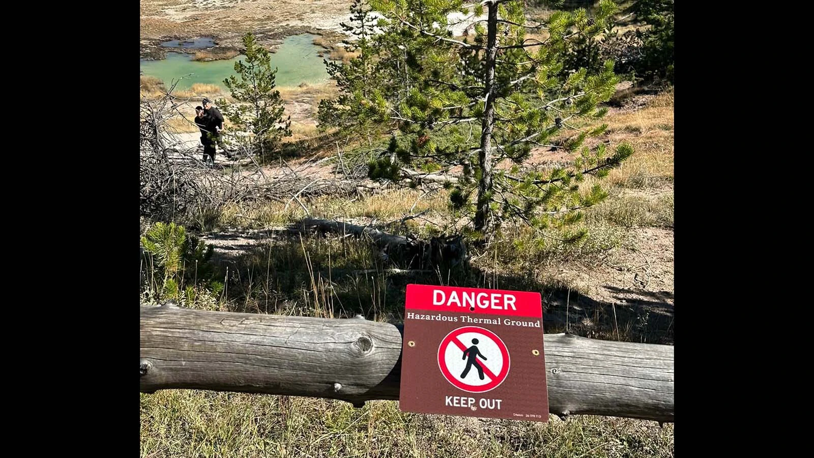 Two tourists, upper left, who blatantly ignored prominent "DANGER" and "KEEP OUT" signs on the boardwalk of a Yellowstone thermal basin.