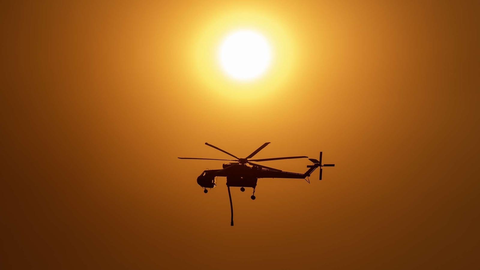 A Sikorsky S-64 Skycrane surveying the fire before it filled its tank in a stock pond. The sky is a deep orange because of the smoke from the fire, the smoke also helping in tamping down the intensity of the sun.