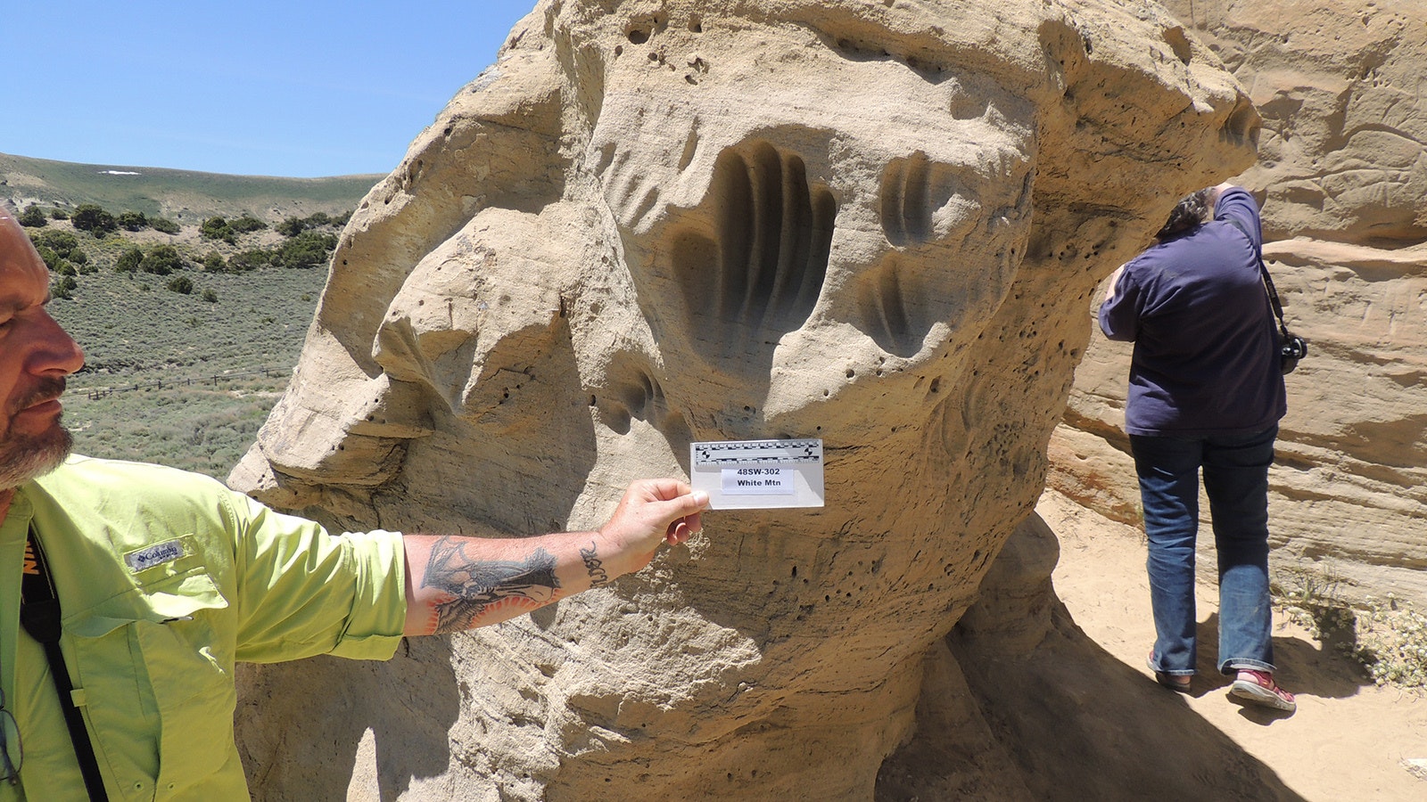 Jim Stewart holds an archaeological scale bar up to a series of hand impressions at the White Mountain Petroglyph Site, 28 miles north of Rock Springs.