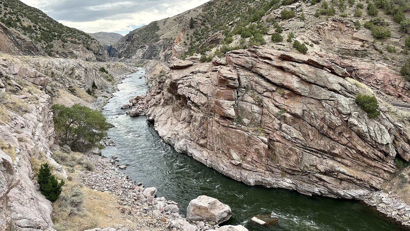 The Great Unconformity at the southern end of the Wind River Canyon. The gap between the black and pink Precambrian granite at the waterline and the juniper-covered Flathead Sandstone above it is 2 billion years of Earth's history that's vanished.