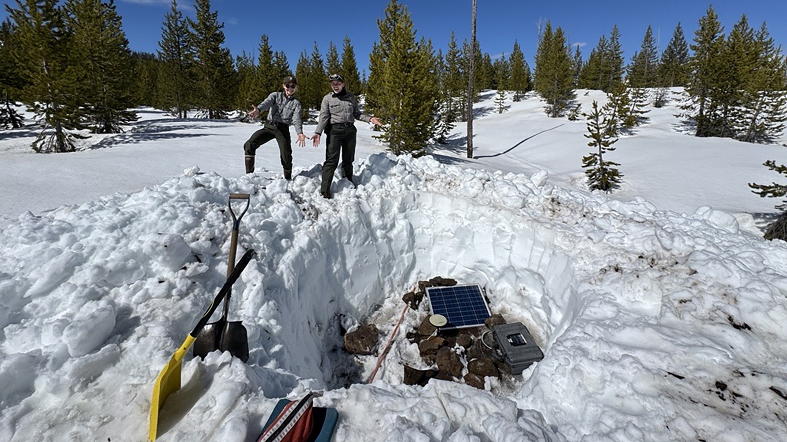 Yellowstone National Park Geology Program team members Samantha Hilburn (left) and Margery Price (right), both Physical Science Technicians, pose with a snow pit dug near Lewis Canyon for installation of a semi-permanent GPS site, installed in collaboration with USGS scientists.