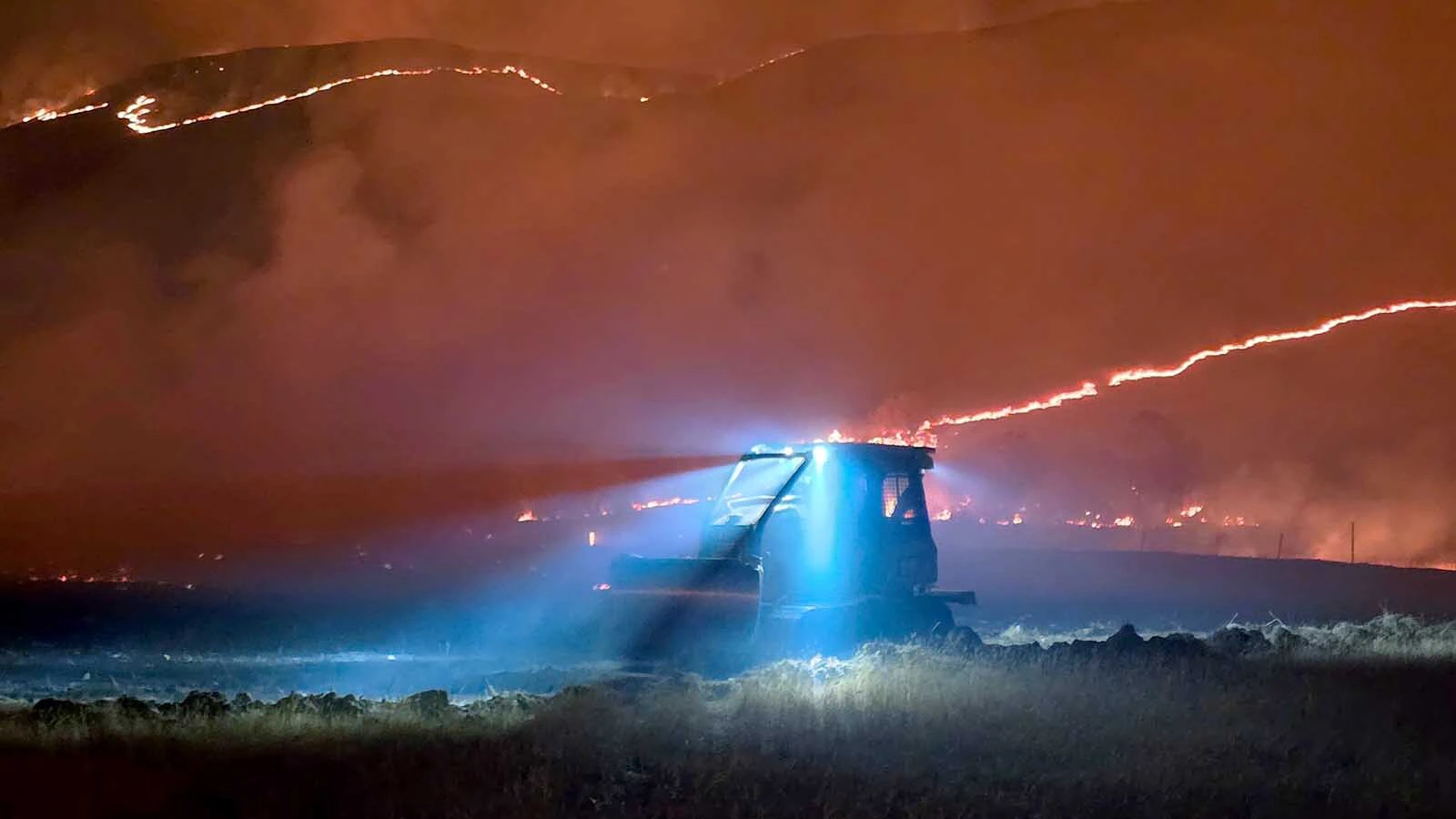Flames creep across the landscape behind Yoder Volunteer Fire Department trucks. The tiny Goshen County department has become an outsized force in Wyoming's wildfire response efforts.
