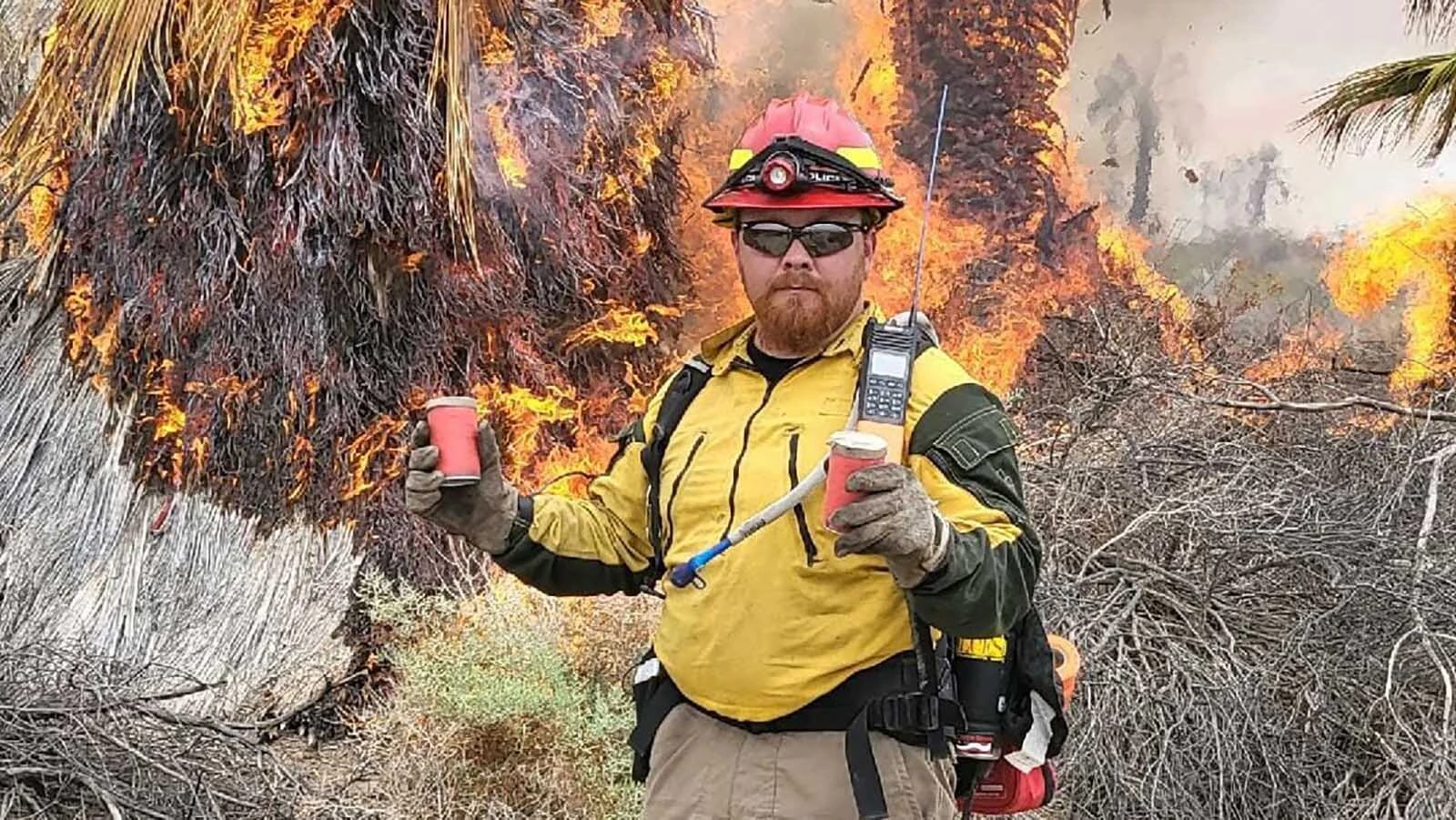 With flames consuming palm trees behind him, Yoder firefighter Shane Tromke pauses during a federal wildfire assignment. 