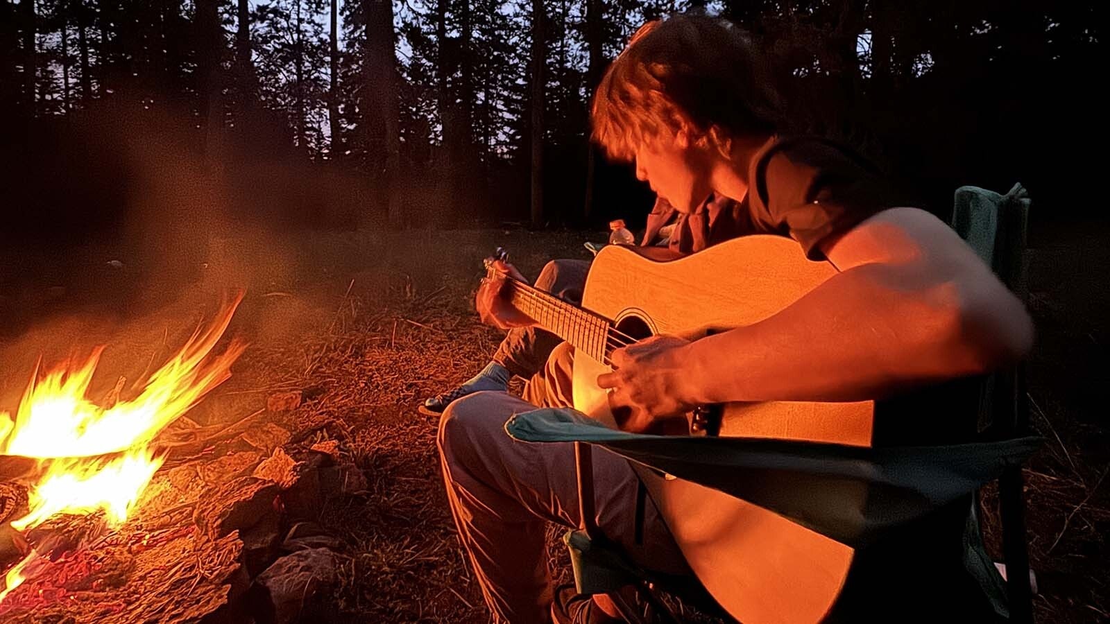 Liam Jordan plays a guitar near a campfire in the Bighorn mountains in 2024.