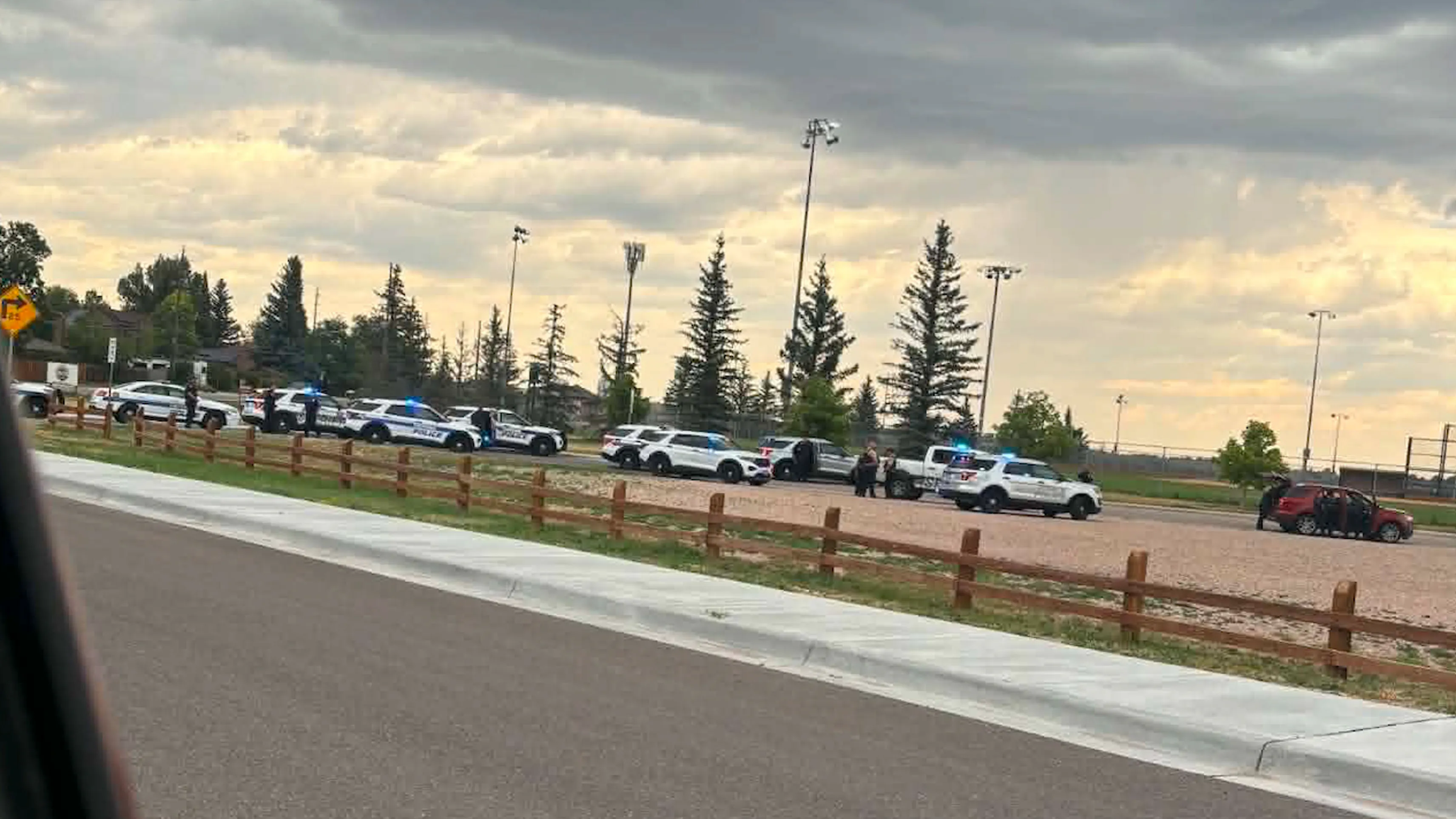 Numerous law enforcement vehicles with emergency lights flashing were clustered near athletic fields east of Ace Hardware, where officers appeared to be investigating and searching vehicles.