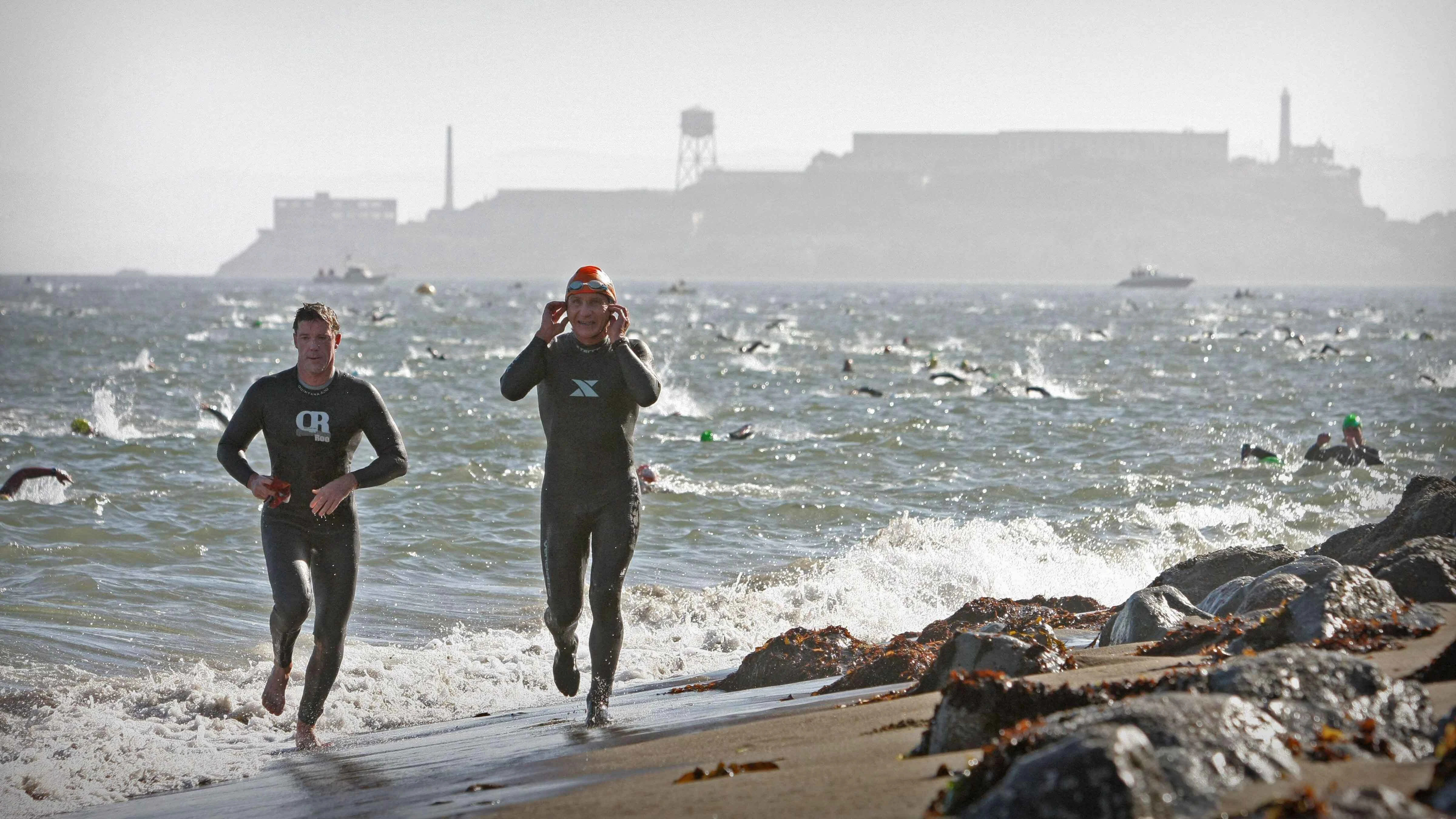 Escape from Alcatraz Triathlon -- Competitors emerge from the surf at Crissy Field after the 1.5 mile swim from Alcatraz Island in background