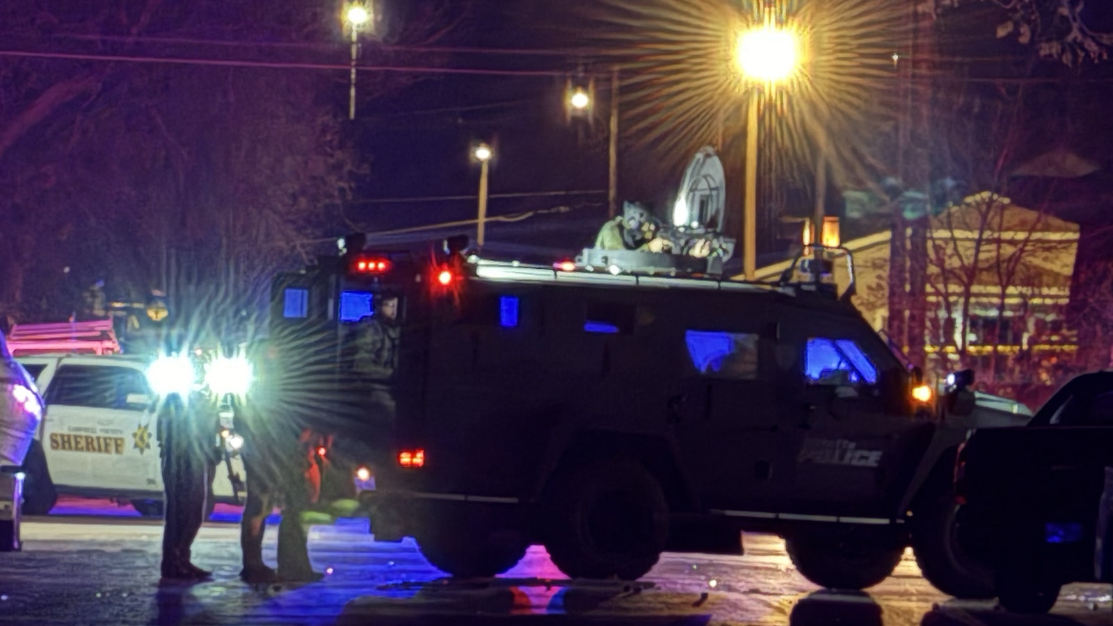 A tactical officer aims a rifle from atop an armored vehicle Tuesday night during a standoff in Sheridan with a man suspected of killing a police officer.