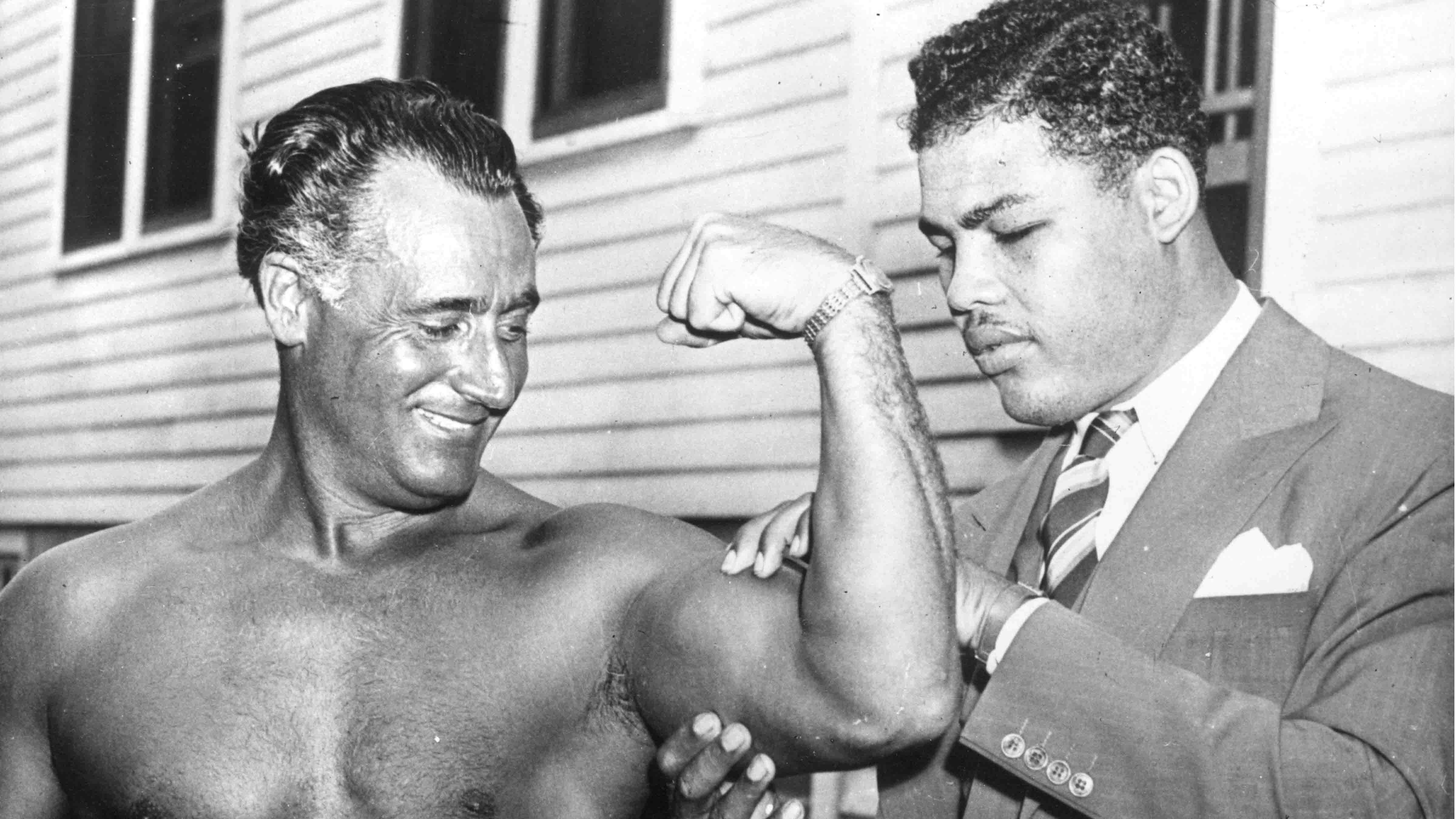 World heavyweight champion Joe Louis (1914 - 1981) admires the flexed bicep of Charles Atlas, considered by some to be the world's most perfectly developed man, at Madame Bey's Camp in Summit, New Jersey.