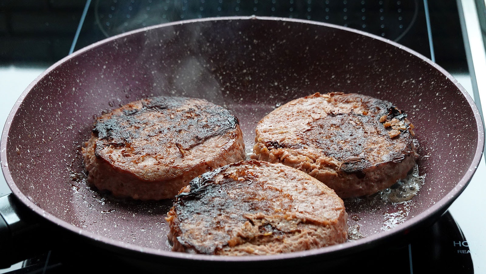Beyond Meat burgers cook in a pan.