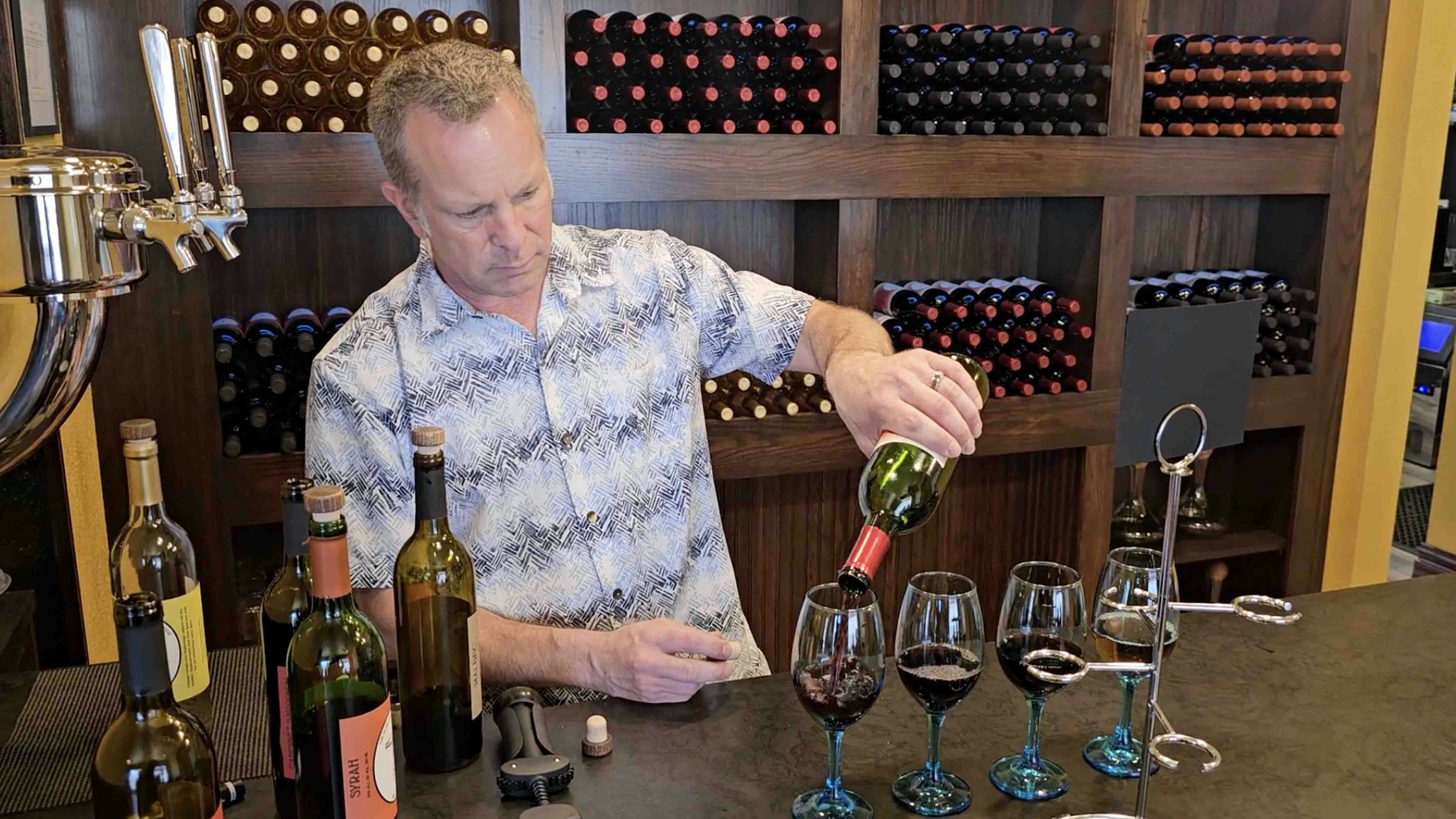 Brandon Erdmann pours glasses of wine for a tasting flight at Blue Stem Wine House. The glasses will go into the spiral holder, along with a notecard that labels each wine in order.