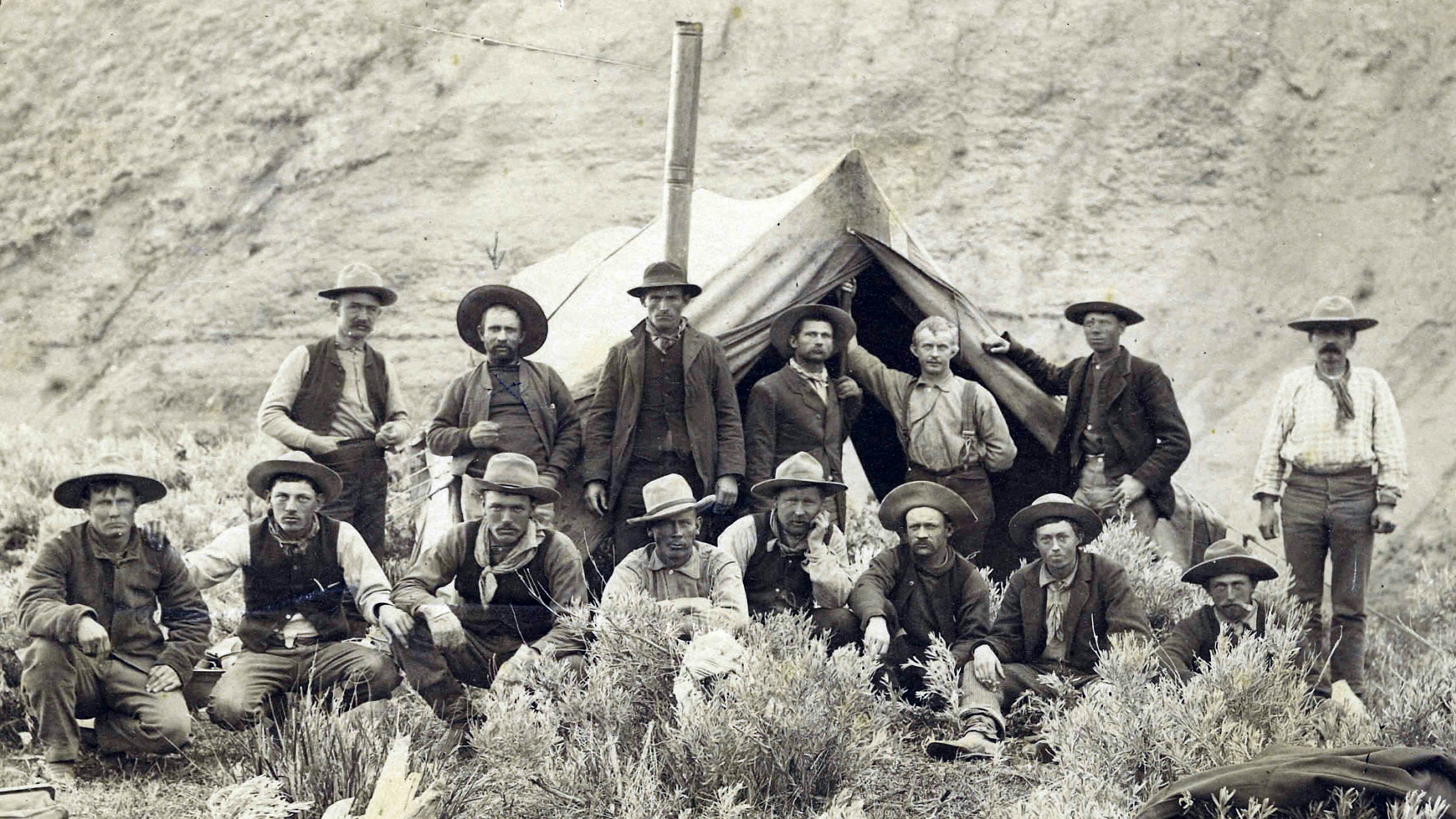Cowboys on the range. Depicts many men sitting in front of a cook's tent in the late 1800s.