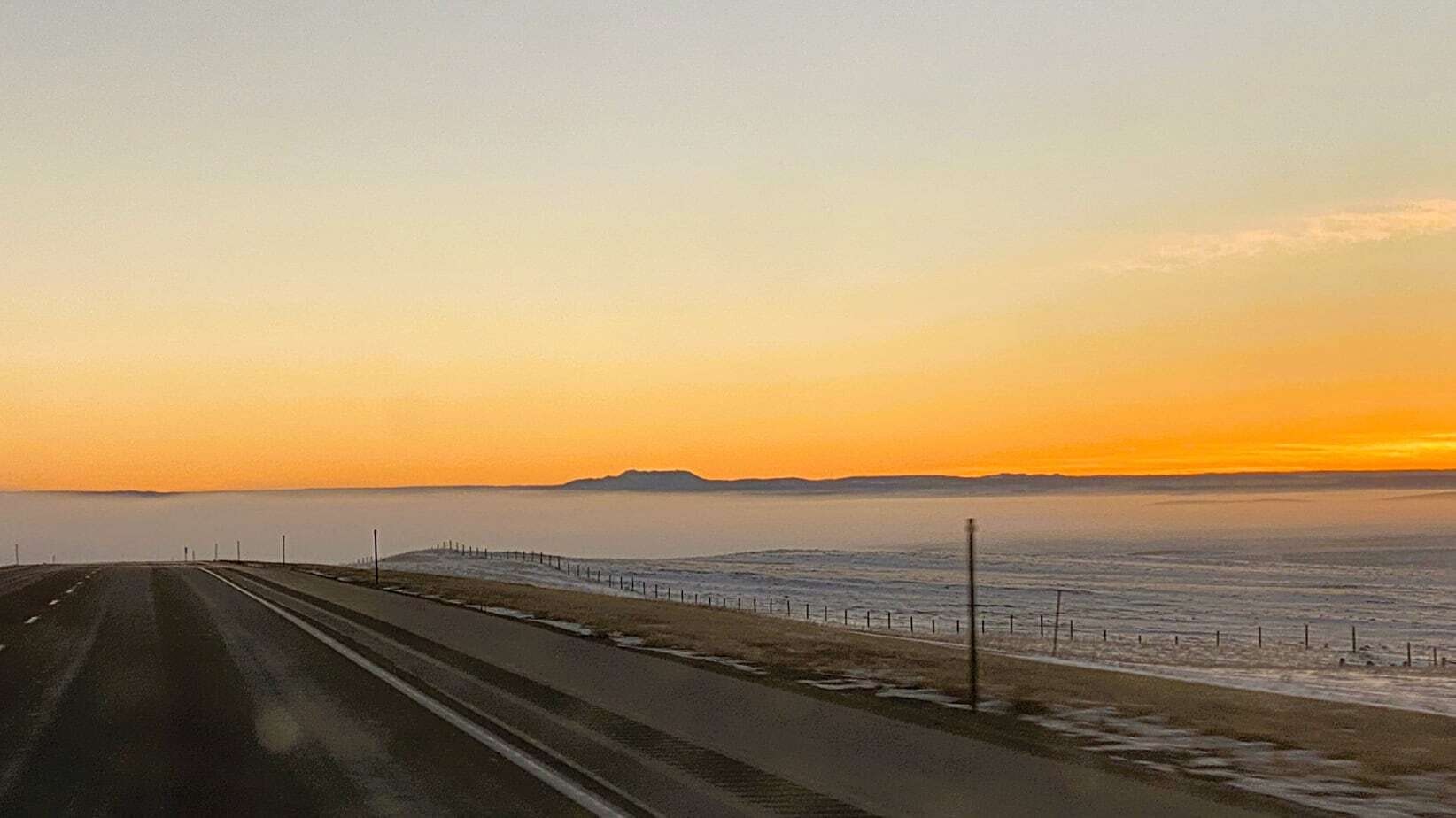 "East of Moorcroft on I-90 as I crested a hill I got this incredible sunrise.  A beautiful silhouette of Inyan Kara Mountain emerging from a blanket of ground fog."