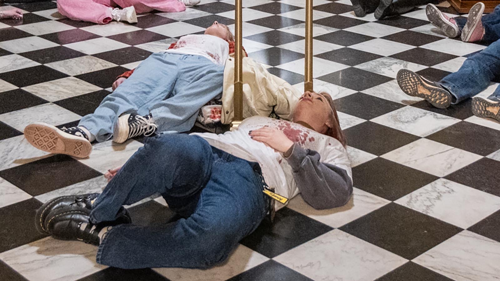 About 20 protesters made up to resemble shooting victims lay on the floor of the Wyoming Capitol on Monday afternoon, Feb. 24, 2025, over a bill that would ban gun-free zones.