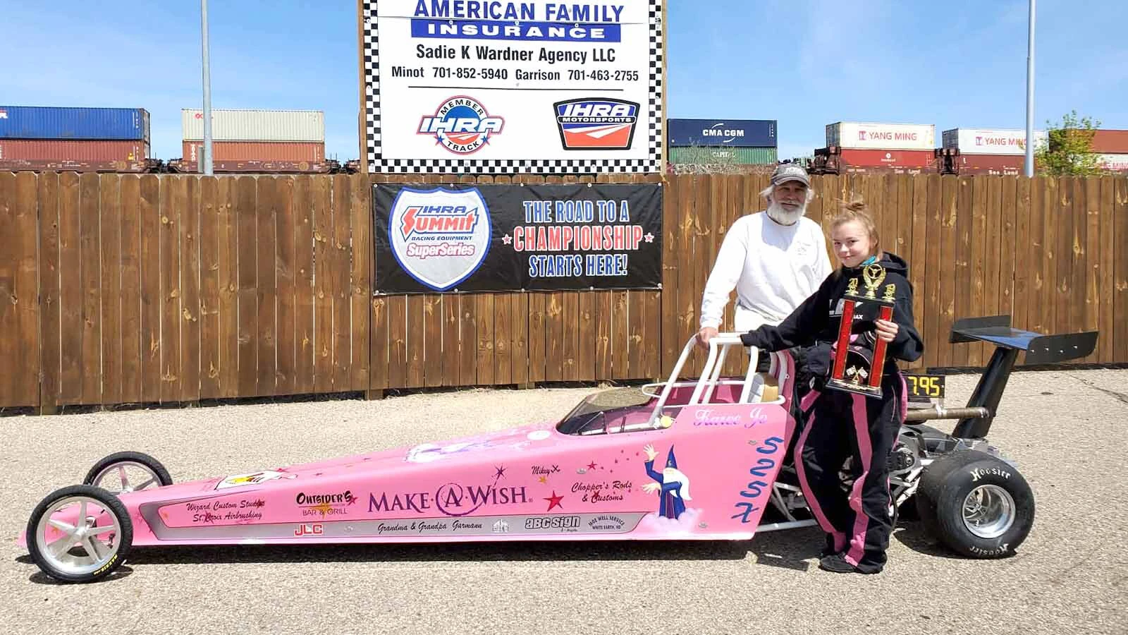 Cary Garmann stands beside a young racer holding a trophy behind a pink dragster at Magic City International Dragway in Minot, North Dakota.