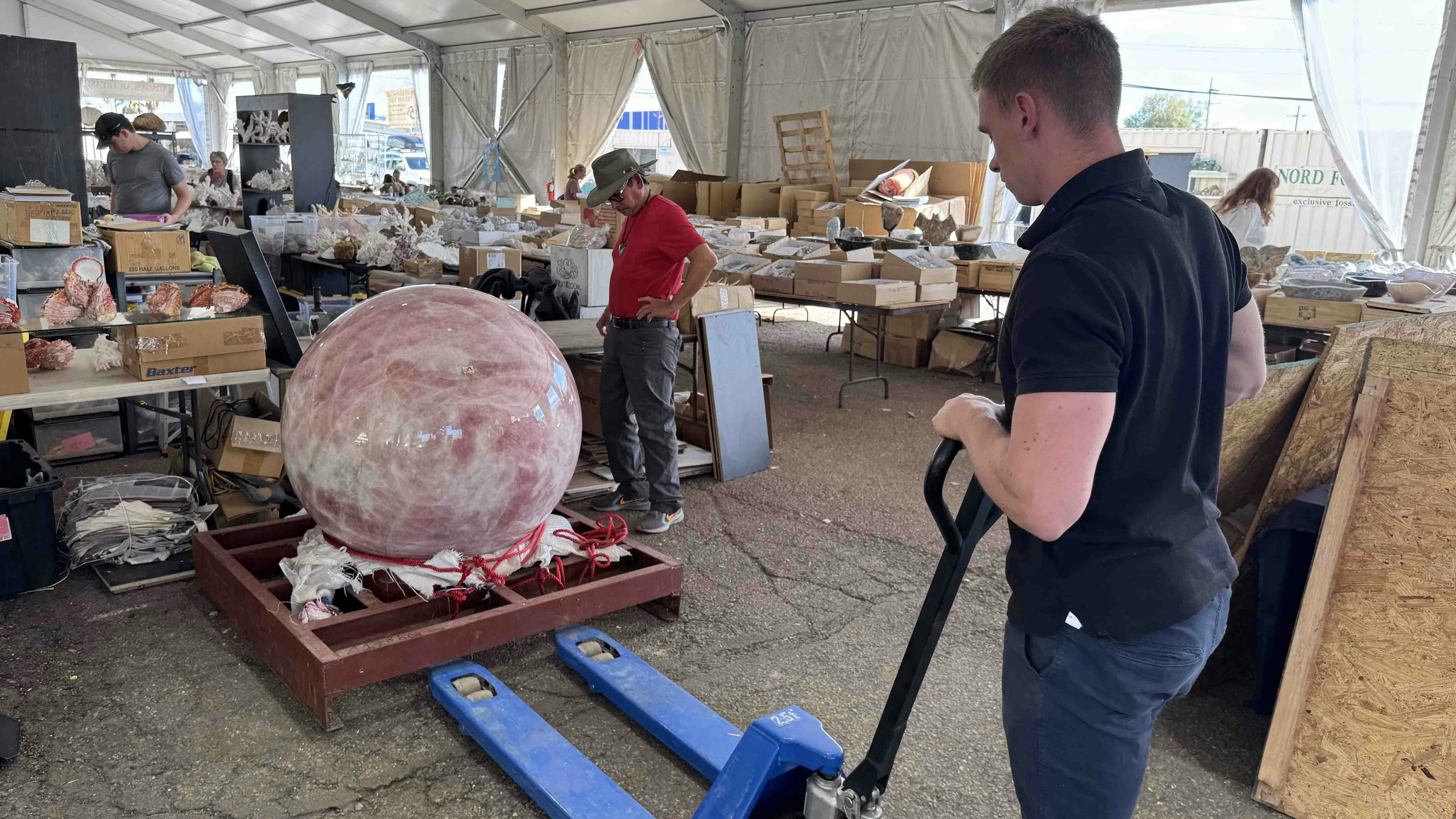 A massive sphere of pink quartz is moved in the Holguin Mexican Minerals booth at the 2025 Tucson Gem and Mineral Show.