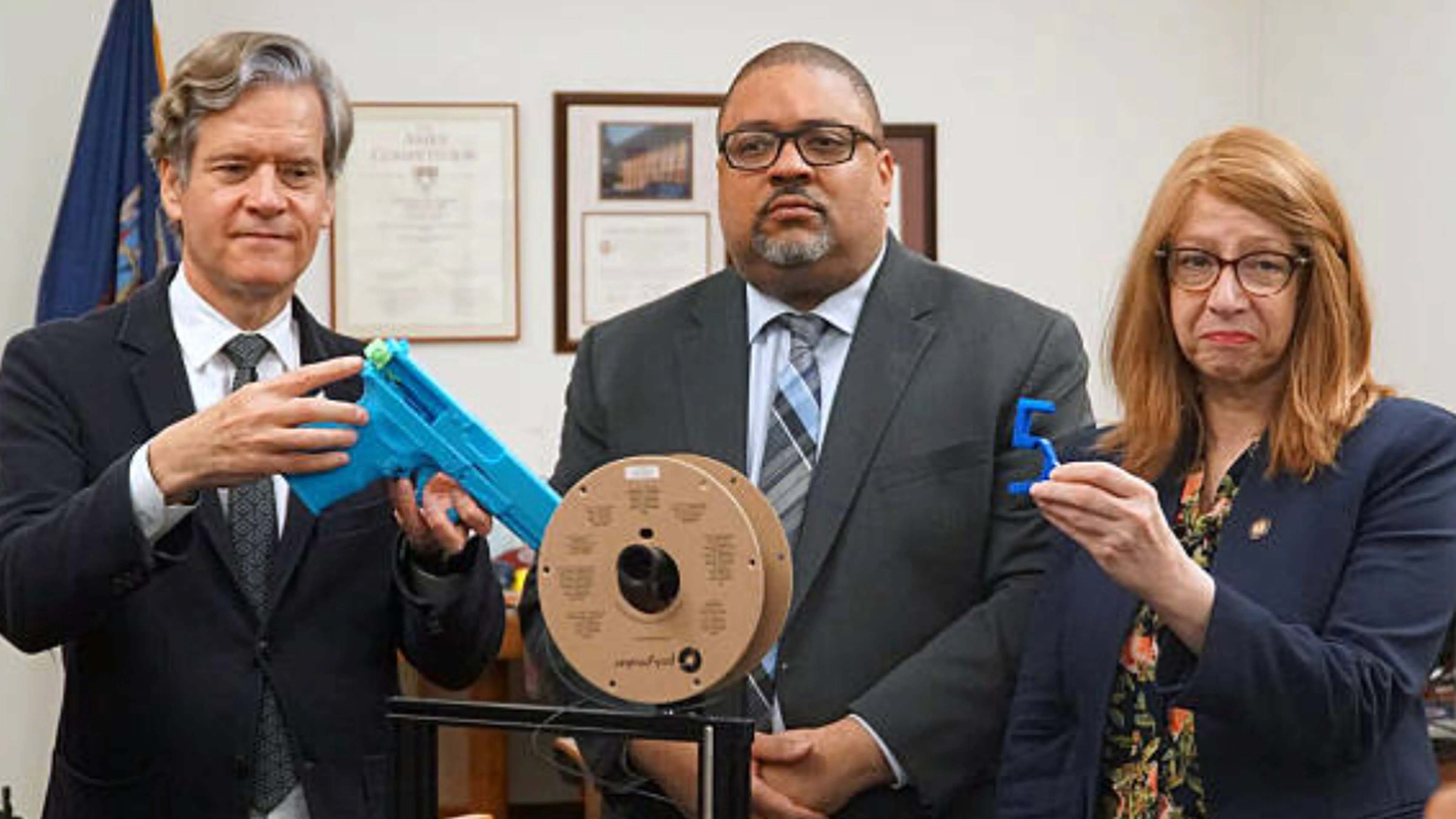 New York state Sen. Brad Hoylman-Sigal, left, holding a 3D-printed ghost gun, stands with Manhattan DA Alvin Bragg, middle, and Assemblymember Linda Rosenthal, who is holding a machine gun conversion device called an auto-sear.