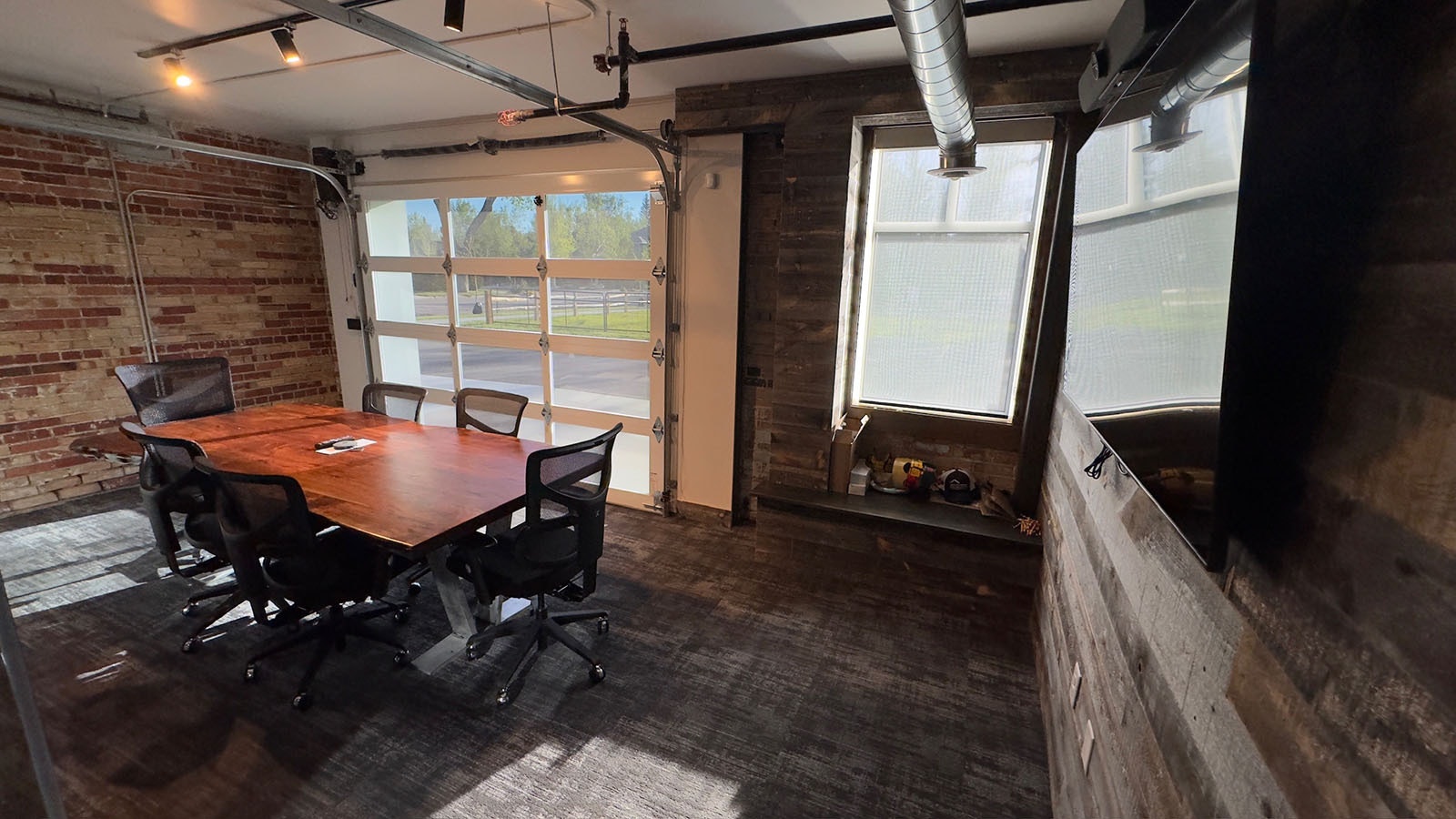The back conference room features a beautiful slab table and a large screen to Zoom morning news budget meetings. The garage door can be opened when the weather's nice.