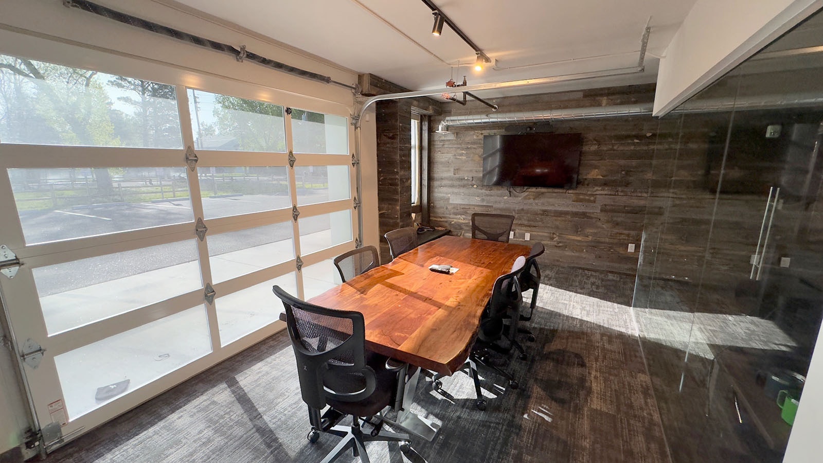 The back conference room features a beautiful slab table and a large screen to Zoom morning news budget meetings. The garage door can be opened when the weather's nice.