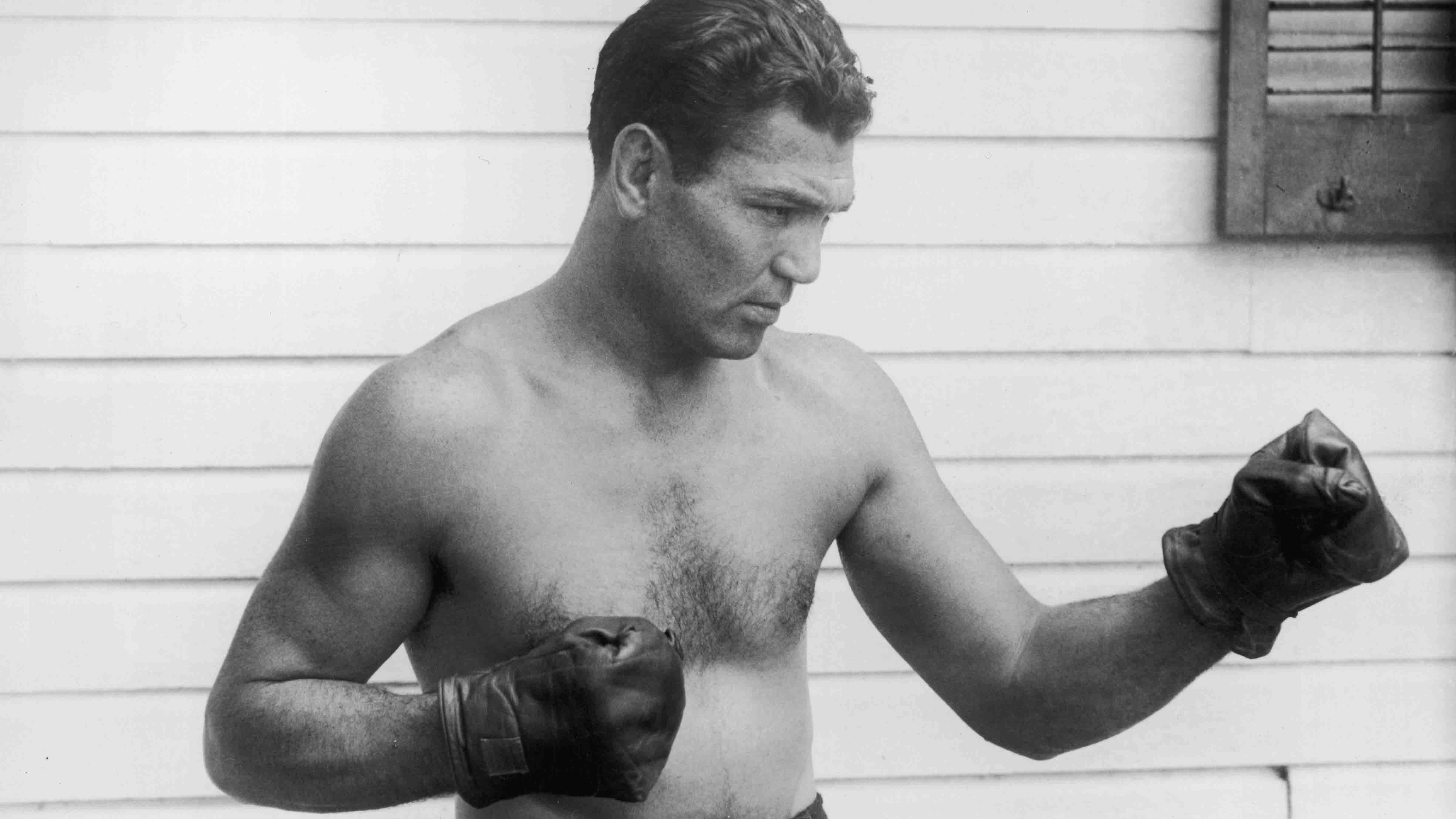 circa 1925: American boxer Jack Dempsey (1895 - 1983) poses outdoors in a fighting stance. He wears boxing trunks and gloves.