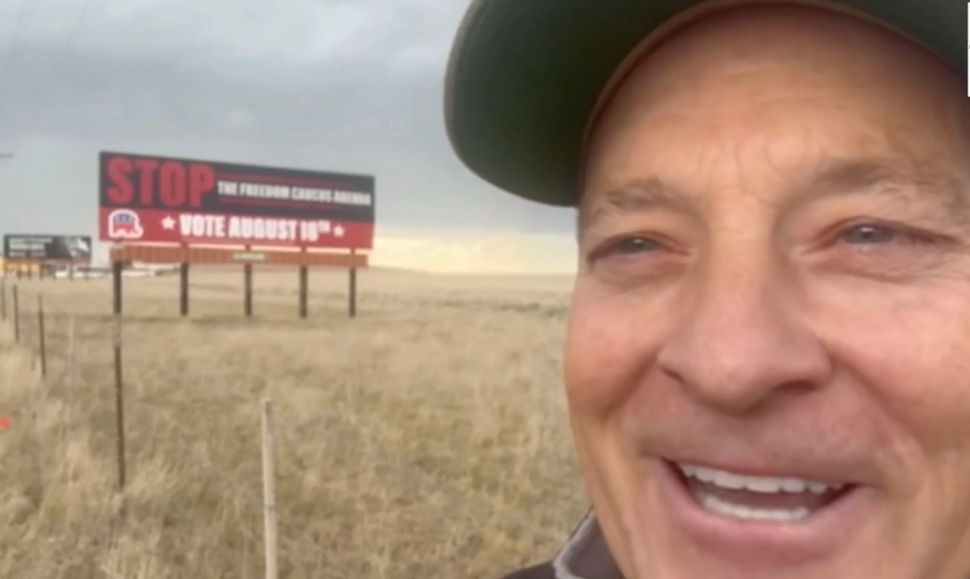 Rep. John Bear, a prominent member of the Freedom Caucus, stands near a billboard urging voters to "Stop the Freedom Caucus agenda."