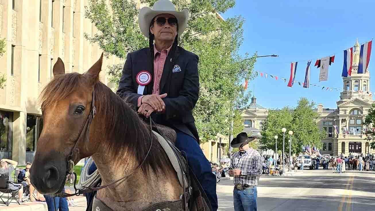 Moses J. Brings Plenty atop a horse named Louie, right before the Cheyenne Frontier Days parade with the Cheyenne Capitol in the background.