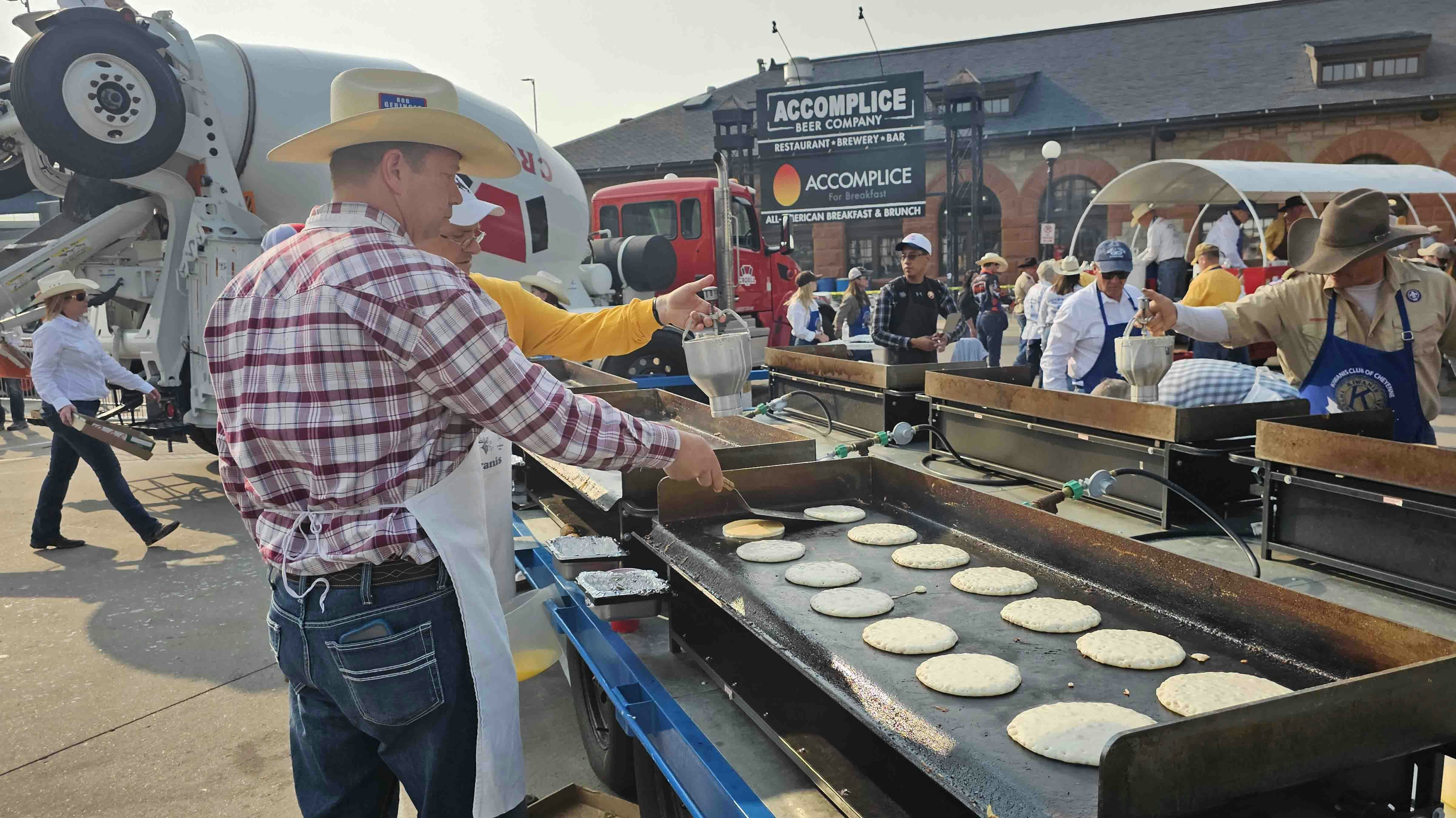 A volunteer flips pancakes just after they have browned on the bottom, while another volunteer puts down more pancake batter.