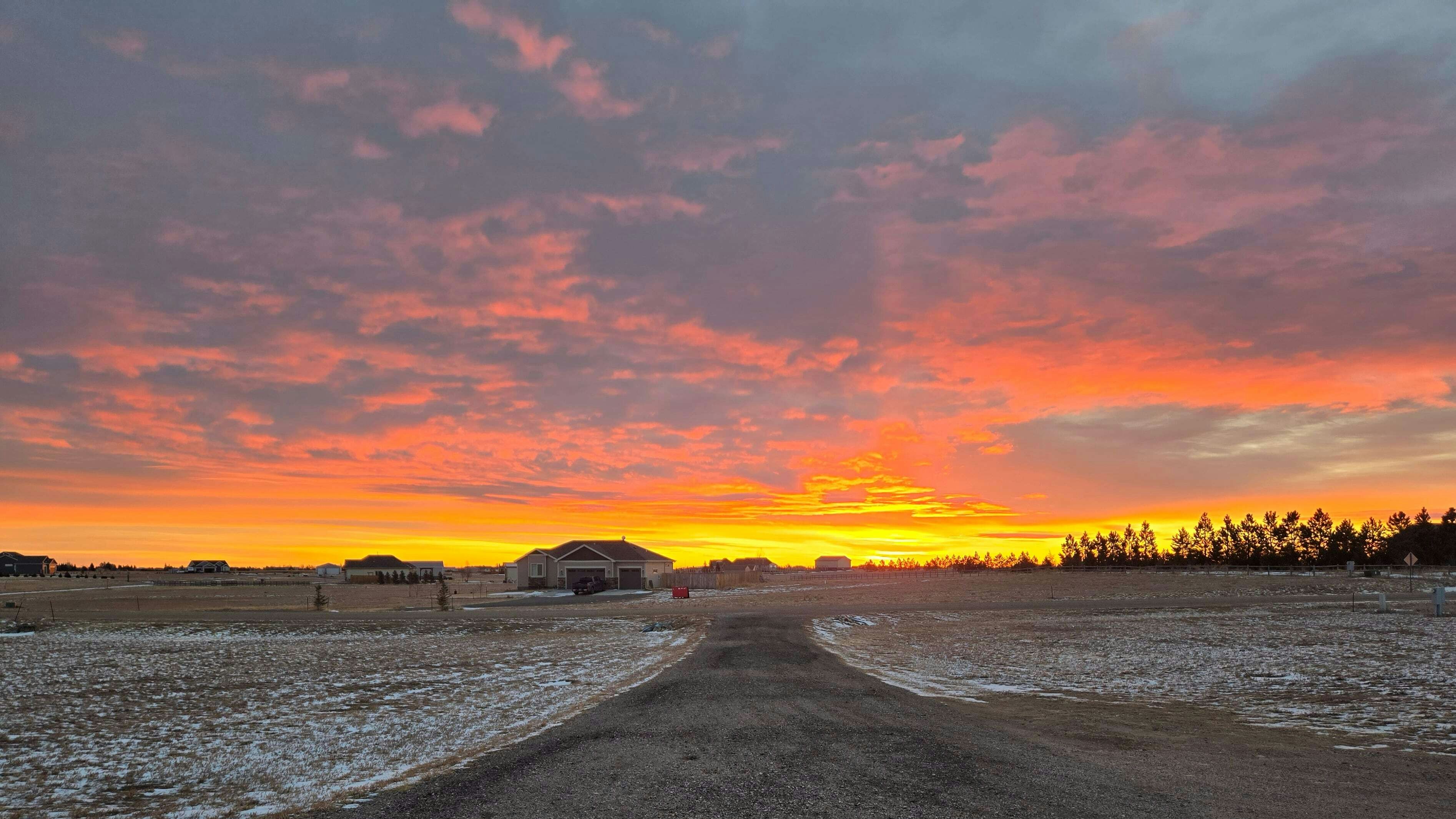 "This view is looking down our driveway to the east. I always know when there is a brilliant and beautiful sunrise because the bright orange glow will sneak in and around the blinds we have on our front window." Cheyenne, WY