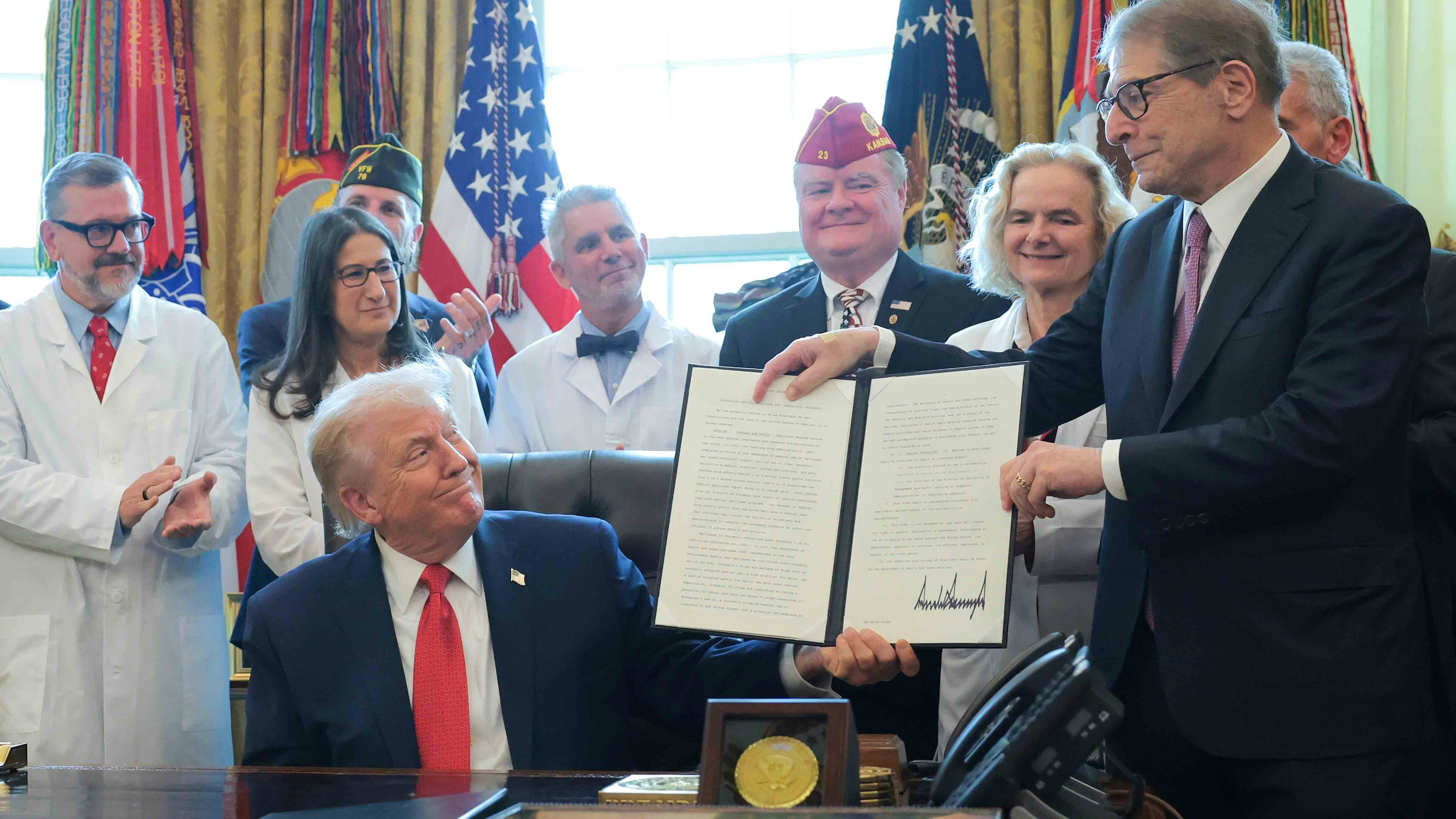U.S. President Donald Trump displays an executive order with Howard Kessler (R) that Trump signed in the Oval Office of the White House on December 18, 2025 in Washington, DC. During the ceremony, Trump signed the order reclassifying marijuana as a schedule III drug.