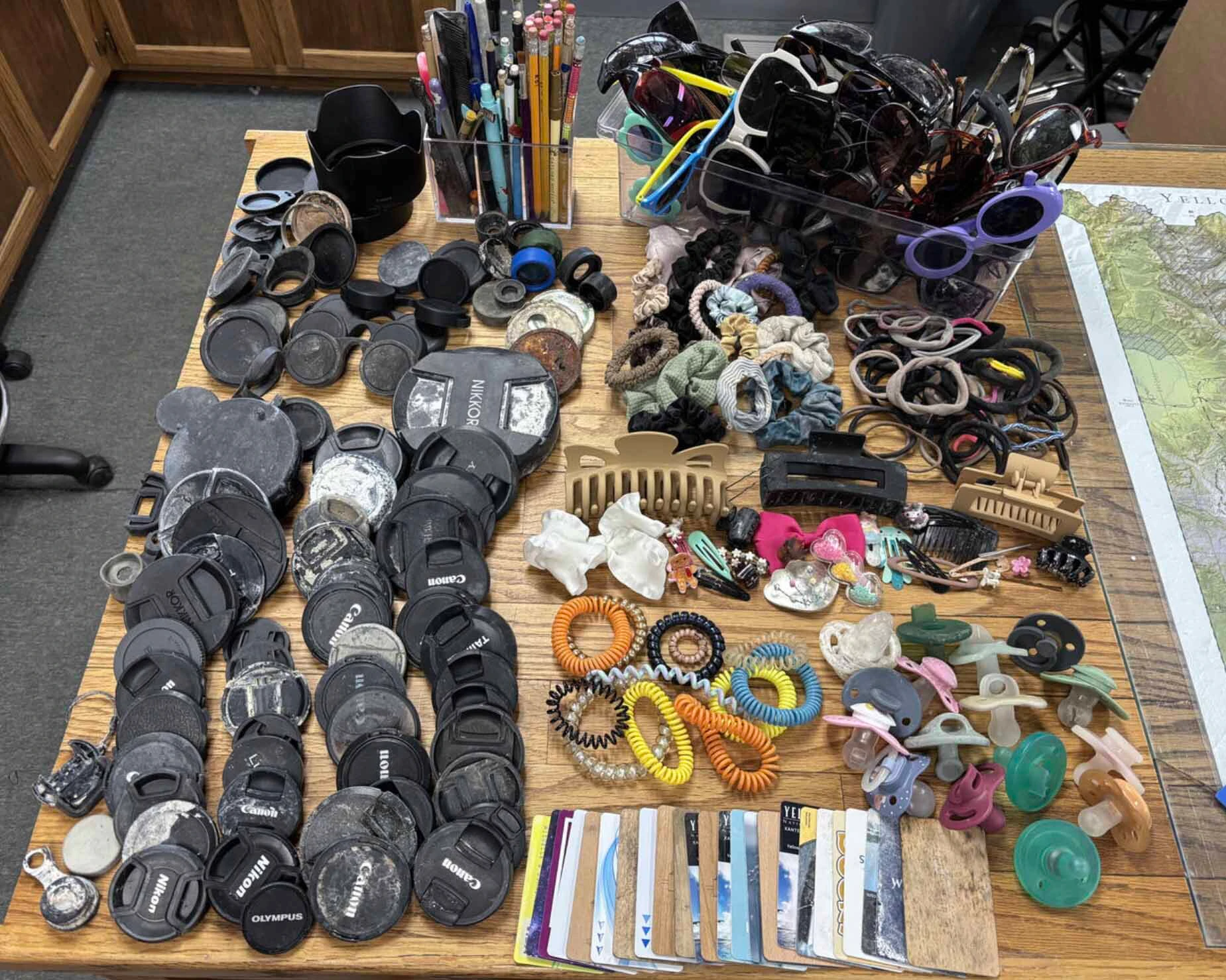Frequent finds collected by the Yellowstone National Park Geology Team from hydrothermal areas during the summer season in 2026: camera lens covers and binocular parts, pens and pencils, sunglasses, hair accessories, hotel keys, and more!