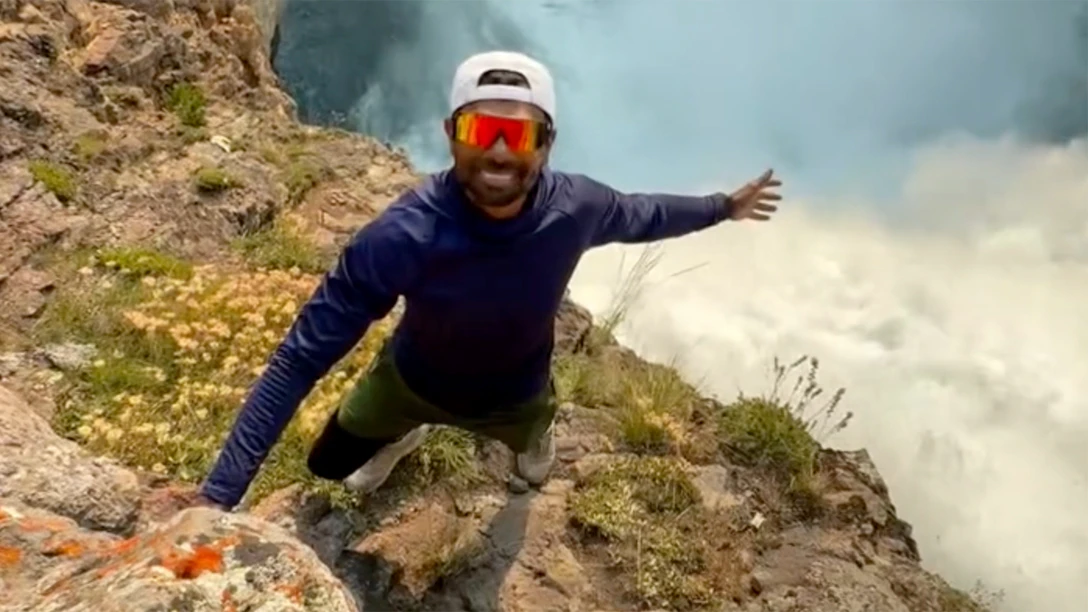 A dimwitted tourist shared a video of himself illegally perched above the 109-foot-tall summit of the Upper Falls of the Grand Canyon in Yellowstone.